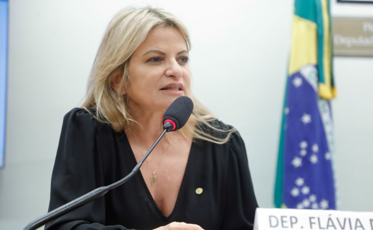 Deputada Flávia Morais fala ao microfone. Ela é loira, tem o cabelo comprido, usa uma blusa preta