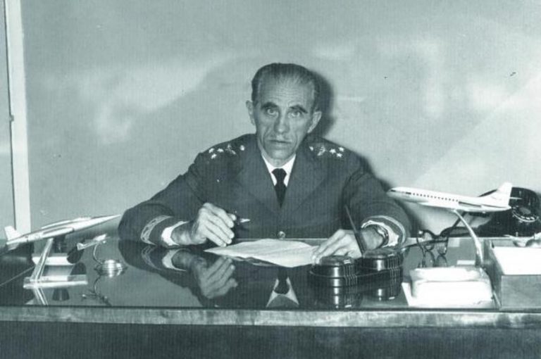 Uma foto antiga de um militar sentado à mesa e olhando para a câmera