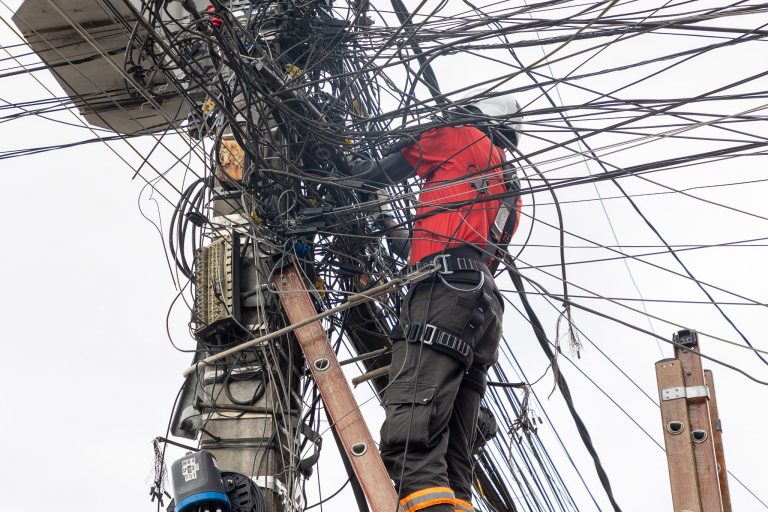 Funcionário em cima de escada em meio a emaranhado de fios em poste de luz