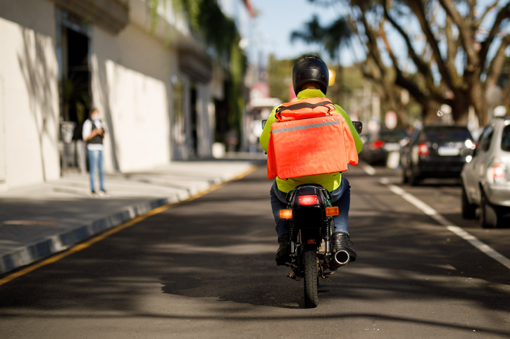 Trabalhador de entrega por aplicativo percorrendo rua em uma moto