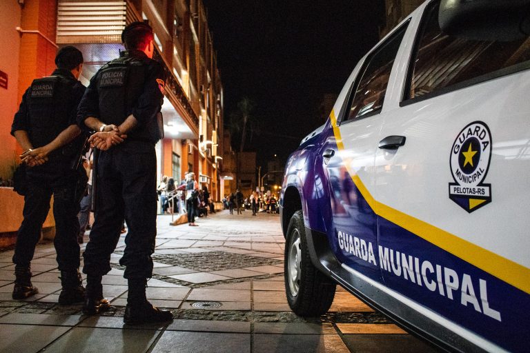 Dois guardas municipais ao lado do carro observando a movimentação da rua