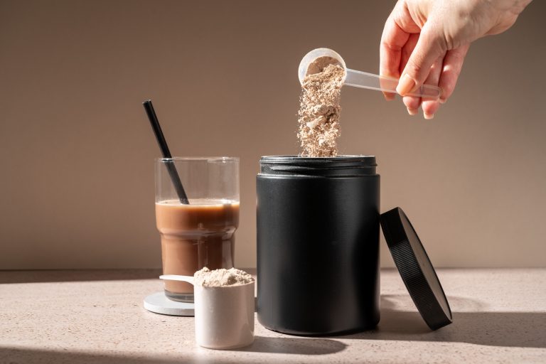 Pote de suplemento alimentar sobre a mesa com um copo com bebida de chocolate
