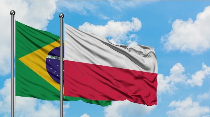 Bandeiras do Brasil e da Polônia balançando ao vento, céu azul com poucas nuvens