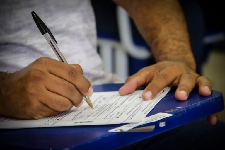 Homem sentado numa carteira fazendo prova