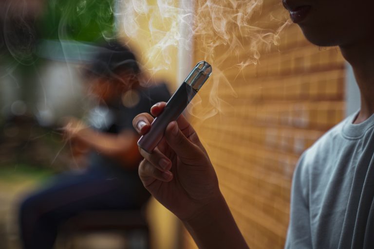 Saúde - Cigarro e bebidas - cigarro eletrônico - Adolescente asiático segura um cigarro eletrônico fumado na mão enquanto está sentado durante o recreio em um canto escondido com seus amigos na escola