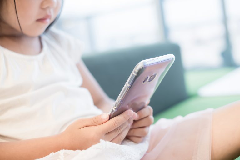 Criança olhando algo no celular que está em suas mãos