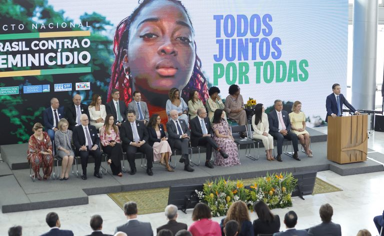 Várias pessoas sentadas num palco ouvem um homem discursar