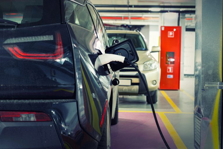 Carro elétrico sendo carregado em ponto de carregamento em garagem