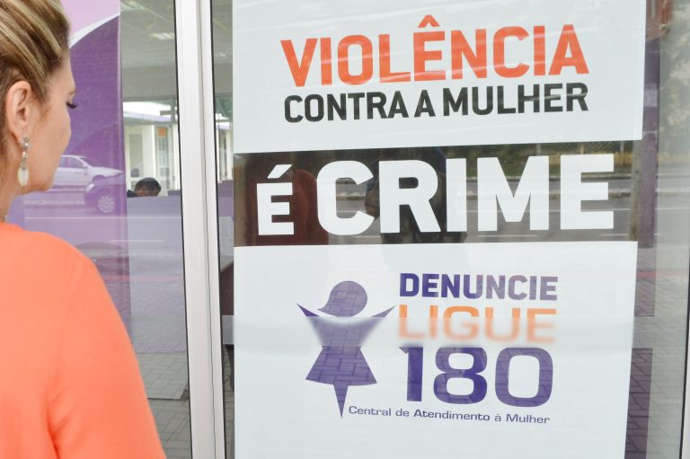 Mulher olha cartaz sobre o Ligue 180, canal de denúncias de violência contra a mulher