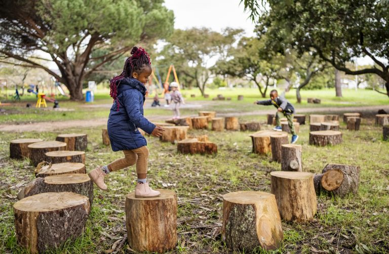 Menina feliz pulando em tocos de árvores no playground