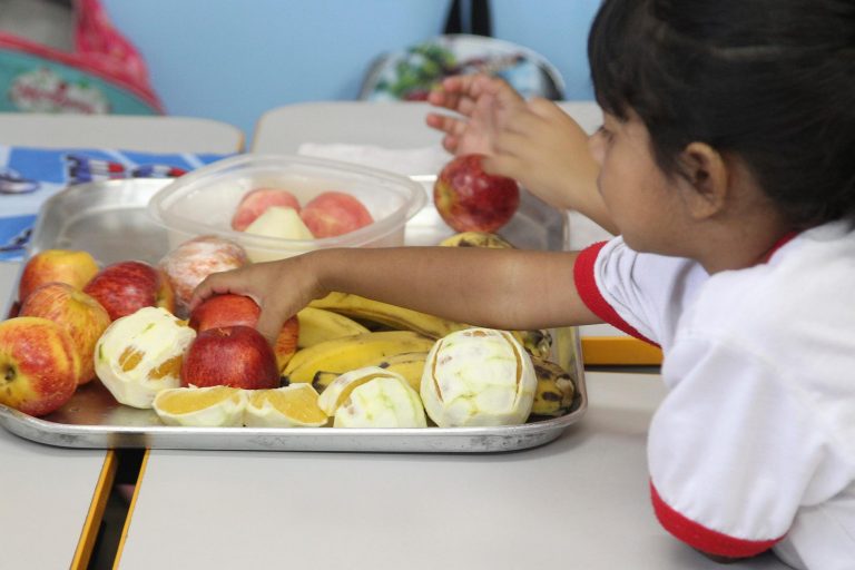 Aluna pegando maçã em bandeja com várias frutas