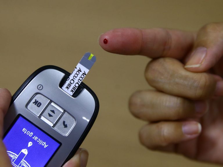 Aparelho medidor de glicose para teste rápido de açúcar no sangue. Pessoa com o dedo furado fazendo o teste.