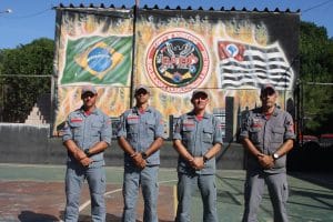 Quatro homens em pé perto de muro com as bandeiras do Brasil e São Paulo