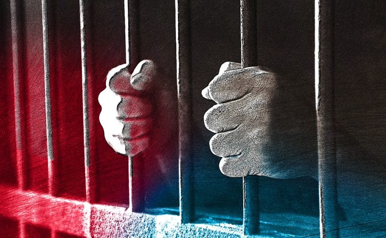 mãos seguram grades de cela