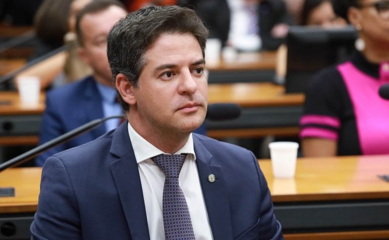 Deputado Ismael Alexandrino está sentado. Ele é um homem claro, tem cabelo escuro, veste um terno azul-marinho e camisa branca