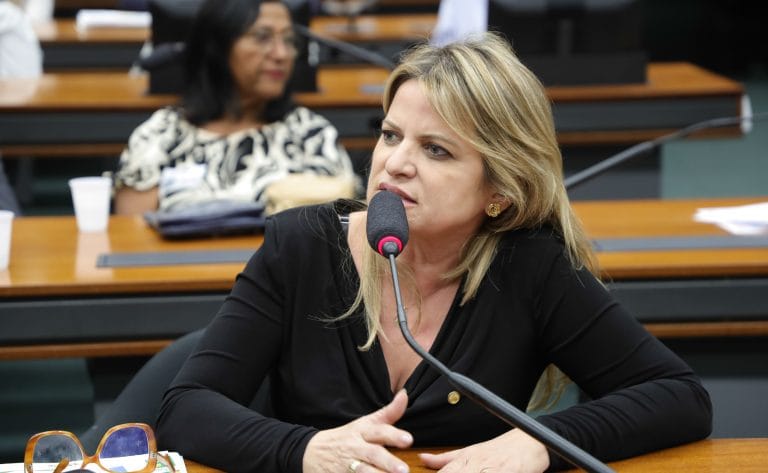 Deputada Flávia Morais fala ao microfone. Ela é loira, tem o cabelo comprido, usa uma blusa preta