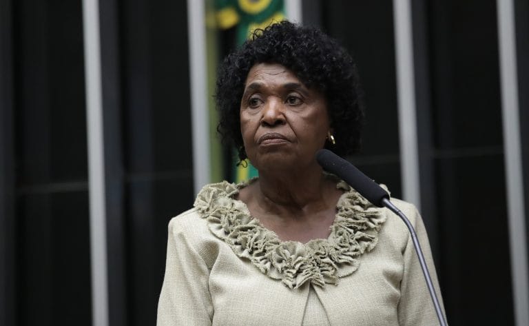 Deputada Benedita da Silva fala ao microfone. Ela é negra, tem cabelo curto e usa um blusa bege