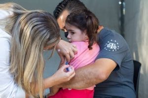 Pai segurando a filha enquanto ela toma a vacina