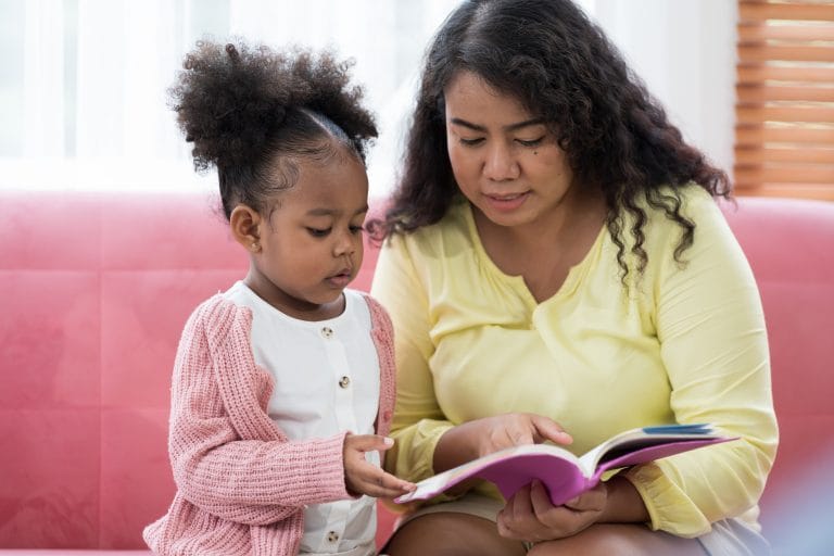 Criança lendo livro com a mãe no sofá de casa - educação - literacia familiar