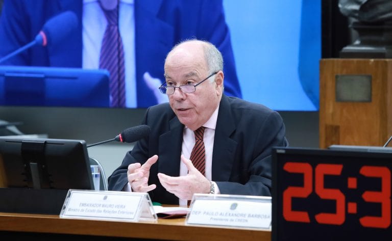 Um homem meio calvo e de cabelo branco fala ao microfone