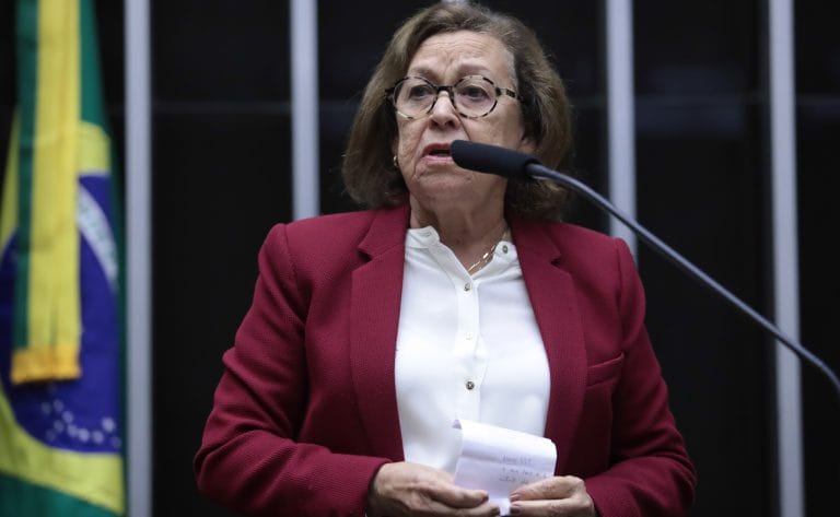 Deputada Lídice da Mata fala ao microfone. Ela é clara, tem cabelo chanel castanho, e usa uma blusa branca e um blazer vinho