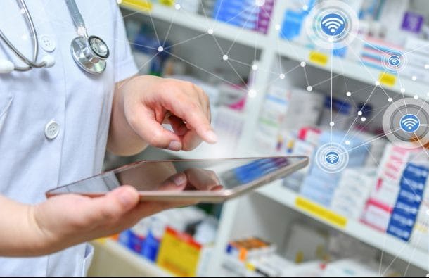Um médico segura um tablet em frente a uma prateleira de remédios
