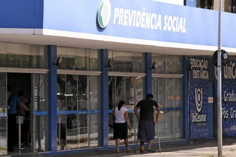 Duas pessoas caminham na frente de uma agência da Previdência Social