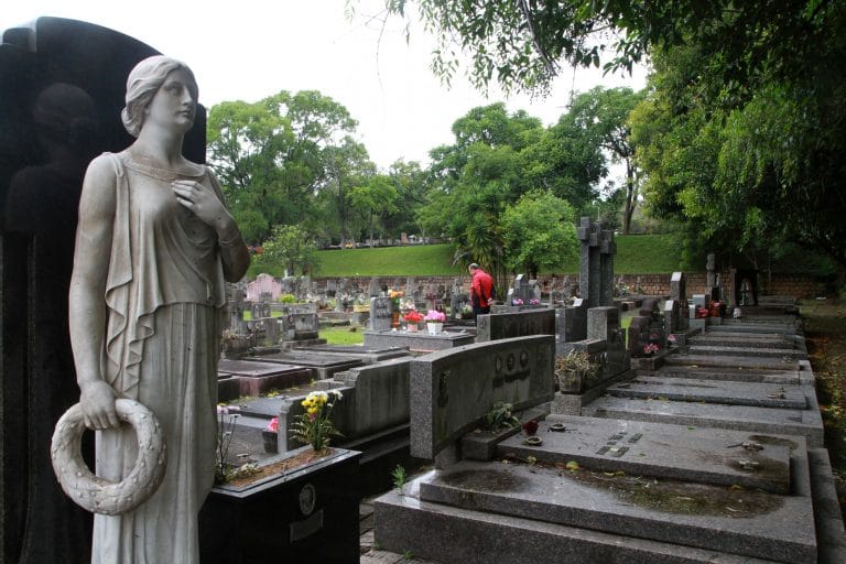 Um cemitério com vários túmulos ao fundo, à direita há a estátua de um anjo