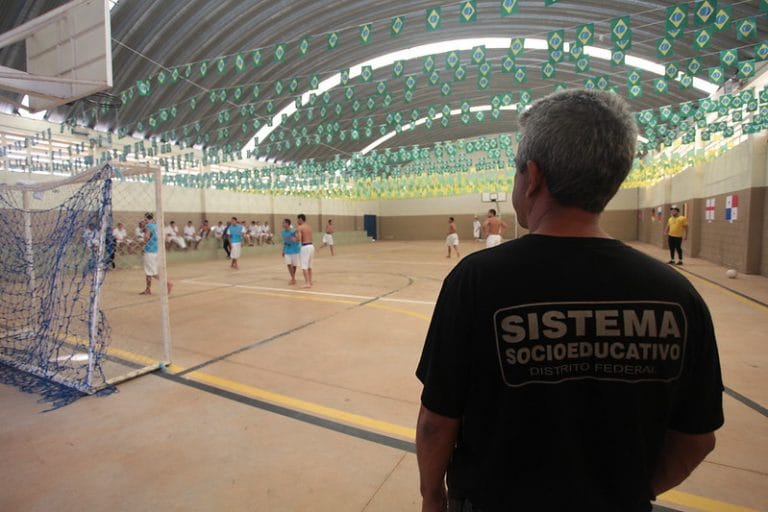 Um homem com camisa preta vigia meninos que jogam futebol num ginásio