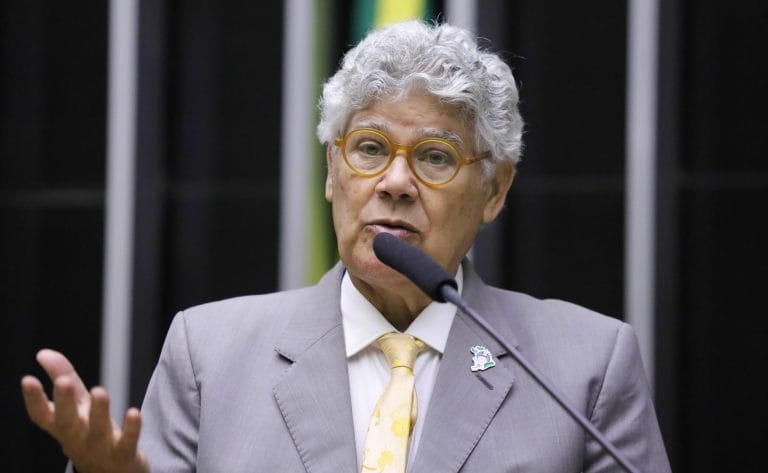 Deputado Chico Alencar fala ao microfone. Ele é claro, tem o cabelo cacheado e grisalho, e usa um terno cinza