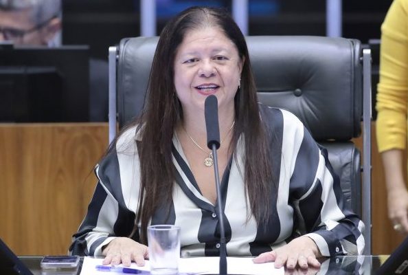 Deputada Laura Carneiro fala ao microfone. Ela é branca, tem o cabelo comprido e escuro, veste uma blusa listrada de preto e branco