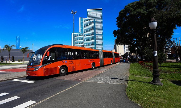 Uma rua com um grande ônibus vermelho trafengando num dia claro