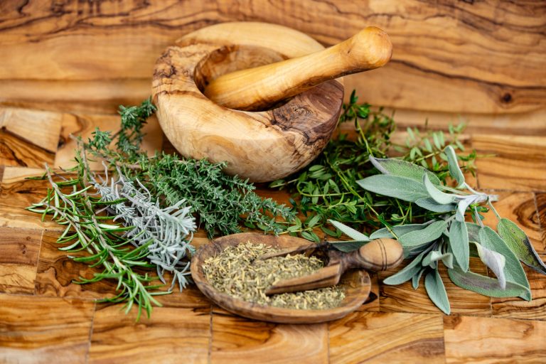 Ervas em cima de uma mesa com um pilão de madeira