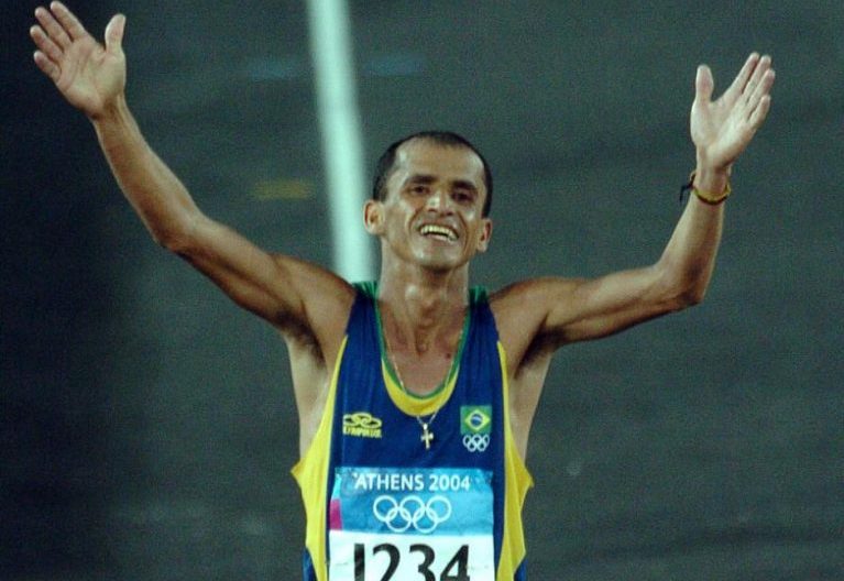 Maratonista está com os braços abertos e levantados. Ele está terminando a prova e sorri