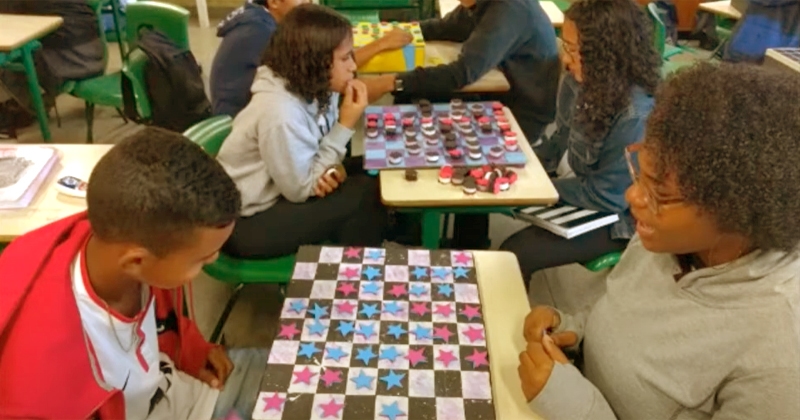 Crianças em sala de aula sentadas na carteira e jogando jogos de tabuleiro numa competição