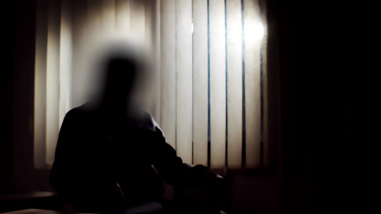 Imagem borrada de uma pessoa num local escuro com uma janela no fundo