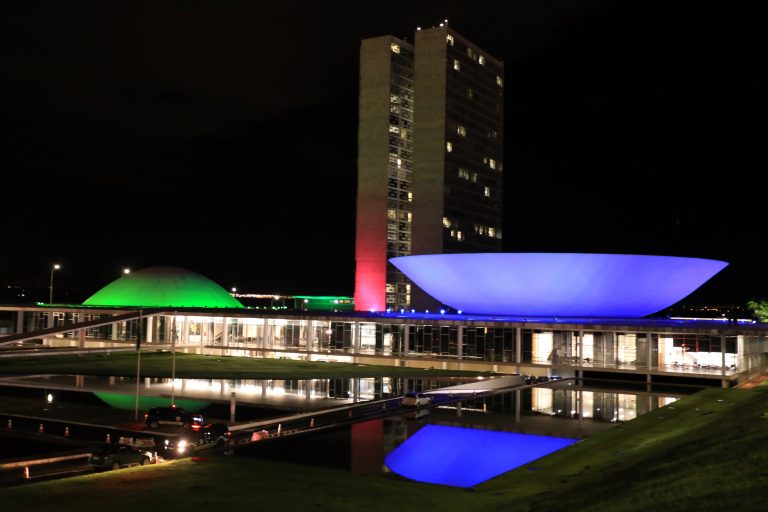 Prédio do Congresso Nacional iluminado de verde, vermelho e lilás
