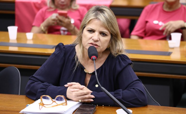 Deputada Flávia Morais fala ao microfone. Ela é loira, tem o cabelo comprido, usa uma blusa preta